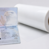 Rollo de película de policarbonato LEXAN™ SD8B24 junto a un pasaporte, utilizado para la fabricación de documentos de seguridad, credenciales y licencias de conducir.